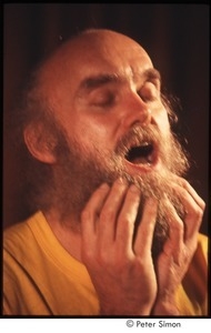 Ram Dass with his hands on his beard, on stage with Amazing Grace