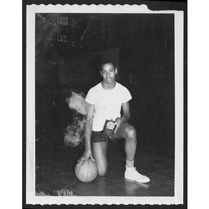Young man poses kneeling with basketball and plaque in gym