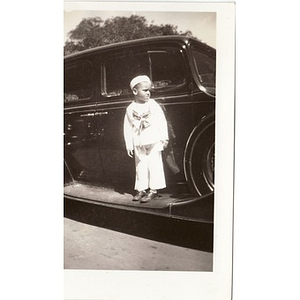 Young boy in sailor costume stands on running board