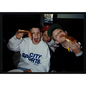 Three boys eating slices of pizza