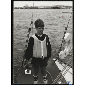 A boy stands on the deck of a sailboat in Boston Harbor