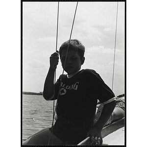 A boy sits on the side of a sailboat in Boston Harbor