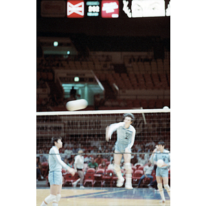 Chinese Men's Volleyball Team member hits a volleyball across the net, with his teammates standing on either side of him