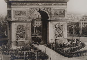 View from above of Marshal Foch and Marshal Joffre leading a military parade under the Arc de Triomphe with military formations around the Arc and civilians crowding the flag-lined streets