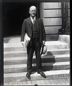 Arthur Brisbane, standing on steps with hat and newspapers in hand
