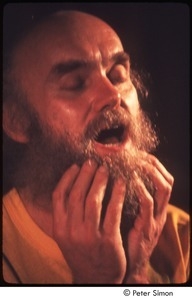 Ram Dass with his hands on his beard, on stage with Amazing Grace