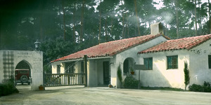 Gateway to white stucco residence, trees and automobile in background