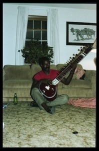 Bobby Davis (?) playing a sitar in a living room floor