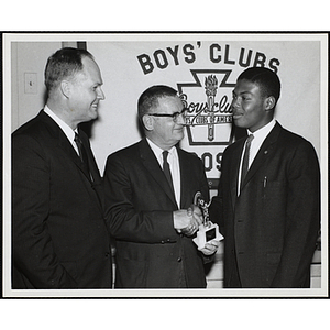 Chris Baker, Boy of the Year, receives a basketball trophy and shakes hands with William G. Mokray while Donald M. DeHart looks on at a South Boston Boys' Club Award Night