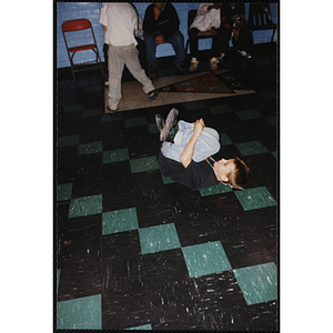 A Young boy spins on his back while break dancing at an open house