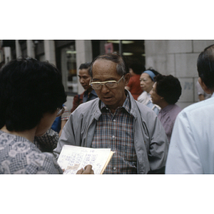 Henry Wong and Suzanne Lee chat in a group with others on a sidewalk in Boston's Chinatown