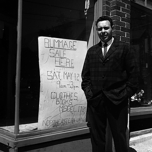 Man stands next to a rummage sale sign