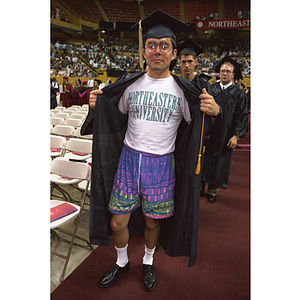 A Northeastern student showing off the outfit, Northeastern shirt and shorts, he wore underneath his graduation gown during commencement