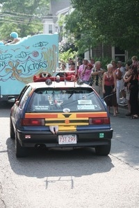 Car in the parade with loud speakers, bumper stickers, and a toy doll hanging from the rear hatch : Provincetown Carnival parade