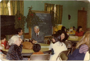 Photograph of a group of adults and children sitting and talking during a Christmas and New Year celebration, [1982-1983].