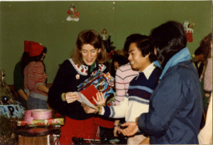 Photograph of two women and a man looking at cards and presents during a Christmas and New Year celebration, [1982-1983].