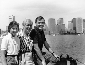 Mayor Raymond L. Flynn, wife Catherine (Kathy) and unidentified child sitting at the East Boston waterfront with Boston Harbor in the background