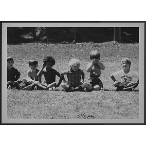 Young boys sitting in a row together on grass