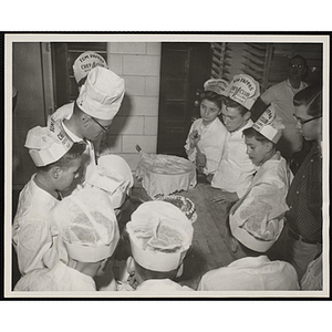 Members of the Tom Pappas Chefs' Club observe a baker decorate a cake in a Brandeis University kitchen