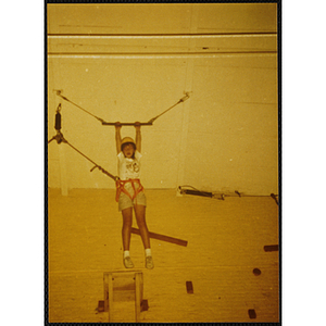 A girl hangs from a trapeze bar in a gymnasium