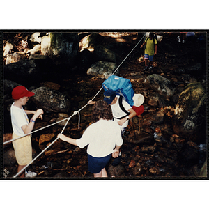A boy holds a rope line to cross a stream along the Piper Trail