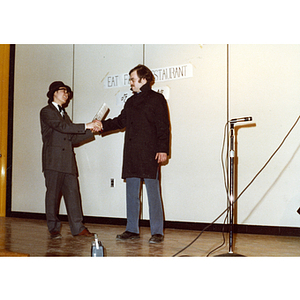 Two men shaking hands in a theatrical sketch set in a Chinese restaurant, performed in the Josiah Quincy School auditorium