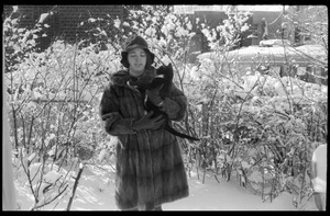 Woman in a heavy fur coat carrying her cat outside after a heavy snow