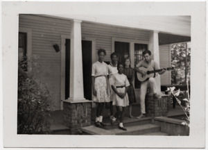 White civil rights worker playing guitar on the front steps of the Freedom House (Kathy Dahl, 2d from right)