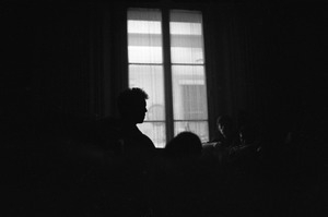 Bob Dylan silhouetted against a window, playing a guitar backstage, Newport Folk Festival