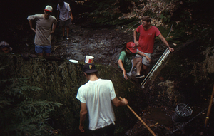 Weir Day 10 August 1993. Sandra Brown (in red baseball cap) climbing through the v-notch. Jay Thoman (in white baseball cap, to left)