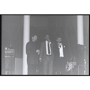 Jerry Steimel, Charlestown Clubhouse director, speaking into a microphone while two unidentified men stand beside him at the Boys and Girls Clubs of Boston 100th Anniversary Celebration Dinner Dance and Auction at International Place, Boston