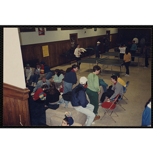 A group of teenagers socialize as other teenagers play table tennis in a hall