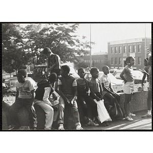 A group of children sit in front of some parked cars