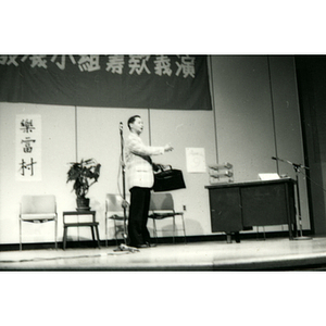 Man holds a briefcase on stage during a skit for the Chinatown Task Force Fundraiser