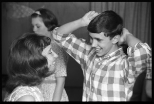 Teenage long hair: boy combing his hair and laughing with a girl looking on