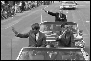 Robert F. Kennedy (left) and Walter Mondale riding in an open car at the Turkey Day parade, waving, while stumping for Democratic candidates in the northern Midwest