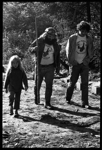 Two men and a young girl walk down a muddy road, Earth People's Park