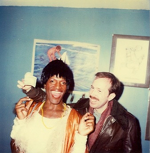 A Photograph of Marsha P. Johnson Wearing a White Feathered Shirt, Posing with Another Person with Their Arm Around Her