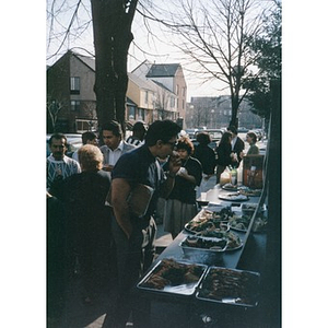 People milling around a buffet table laden with food on a sidewalk in the Villa Victoria neighborhood.