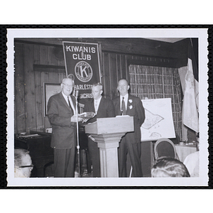 Three men standing at the podium for an award presentation during the Kiwanis Club's Bunker Hill Postage Stamp Luncheon