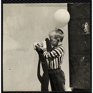 A Boys' Club member writing a wish on a card tied to a balloon. A caption on the back of the photograph states "Balloon raising"