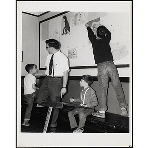 An art instructor and his three students from the Charlestown Boys' Club, one of them pinning up his painting on a board