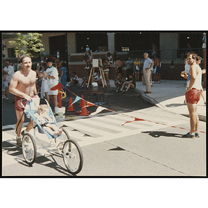 A man pushing a child in a stroller runs in the Battle of Bunker Hill Road Race