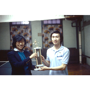 Champion of the men's table tennis stands with Suzanne Lee, both of them holding his trophy