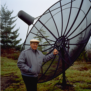 Dr. Roy H. Beaton standing beside a satellite dish