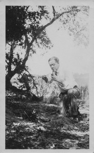 Henry Wilder Foote kneeling by a campfire, lighting his pipe