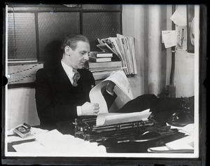 Walter Winchell, seated at his typewriter, smoking a cigarette and reading copy of his column