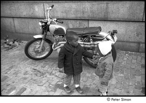 Young boy and girl with a lollipop, standing in front of a motorcycle