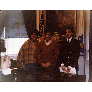 Carmen Pola (?) stands with two men in an office