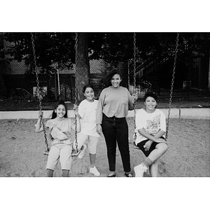 Four unidentified girls posing at the swing set in a playground.